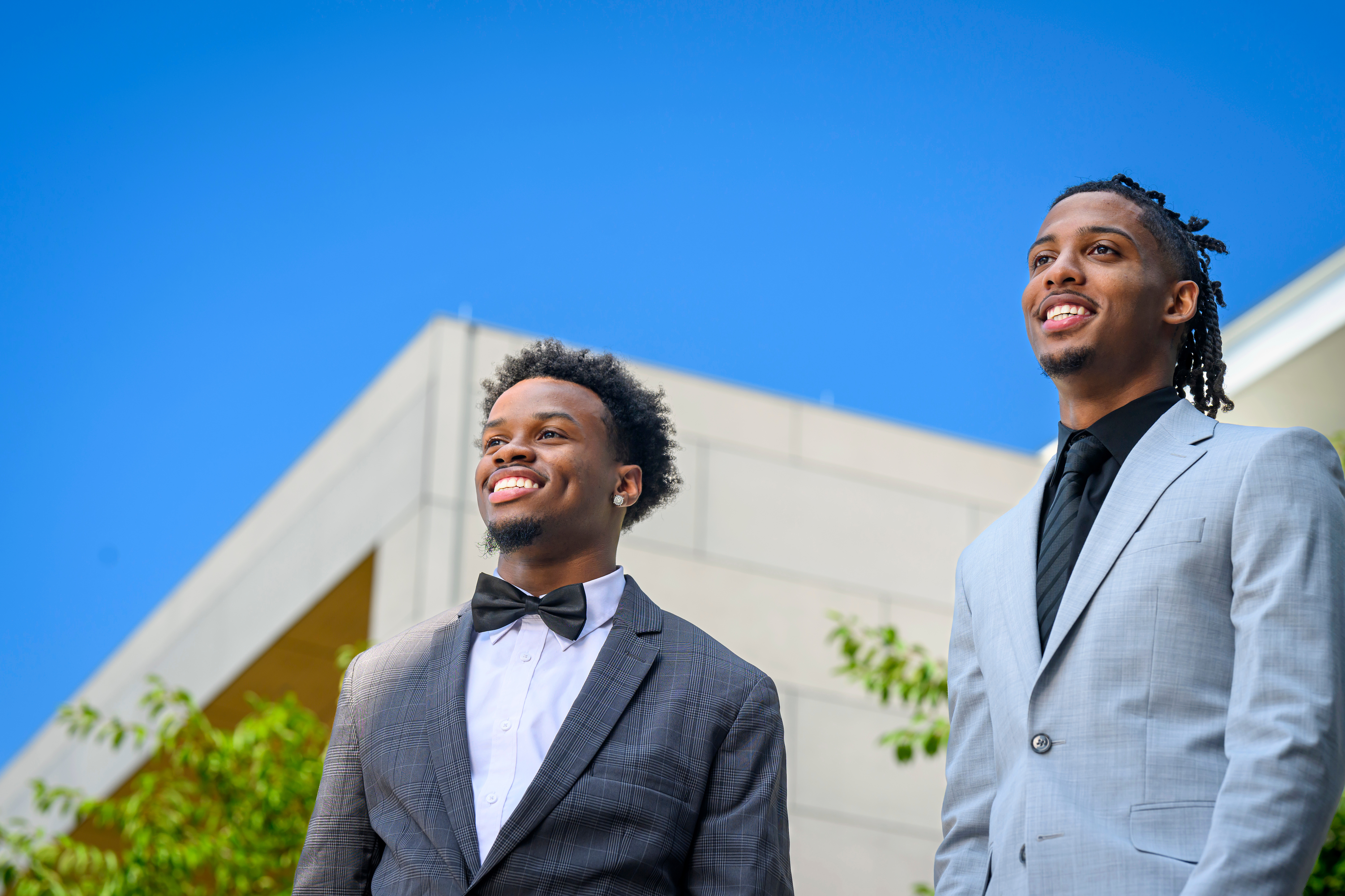 Young black men wearing suits against a blue sky